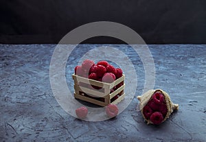 Raspberries in red color in a small wooden box and with a jute sack filled with the same fruit photo