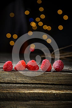 Raspberries in a row on a barn wood board with lights in the background