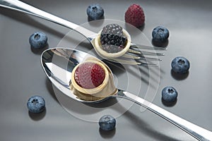 Raspberries, strawberries, blackberries and blueberries in a waffle basket on a spoon and fork. Dessert and vitamins. healthy food