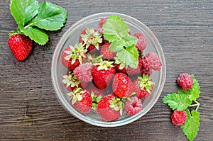 Raspberries with strawberries in a bowl on a brown wooden table with mint leaves