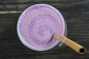 Raspberry banana smoothie with a bamboo straw on a wooden table, closeup, top view