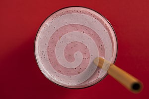 Raspberry banana smoothie in glass on a red background, closeup, top view