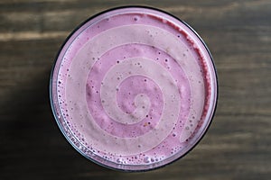 Raspberry banana smoothie in glass on a wooden table, closeup, top view