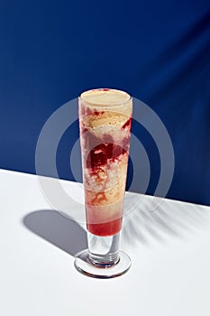 Raspberry and banana smoothie over white and blue background. Palm leaf with sunshine and hard shadow. Fruit yogurt or shake drink