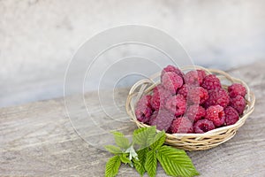 raspberry berries lie in a wicker wooden basket on a gray table, fresh berries for a healthy diet, pink berries and green leaves,