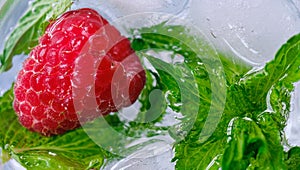 raspberry berry and green mint leaves in ice water closeup from top view