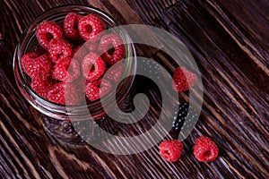 Raspberry and blackberry sweet organic juicy berries in single glass jar on dark wooden table