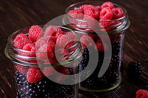 Raspberry and blackberry sweet organic juicy berries in two glass jars on dark wooden table