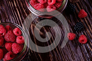 Raspberry and blackberry sweet organic juicy berries in two glass jars on dark wooden table