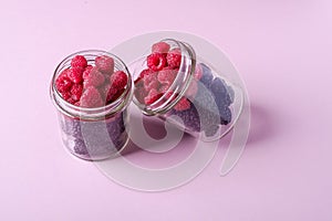 Raspberry and blackberry sweet organic juicy berries in two glass jars on pink paper background, copy space