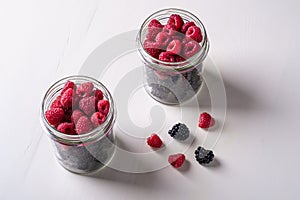 Raspberry and blackberry sweet organic juicy berries in two glass jars on white wooden table background