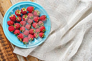 Raspberry in blue dish and in front of white fabric on old vi