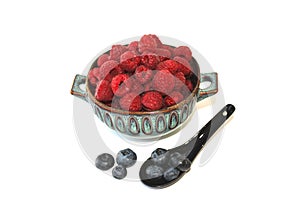 Raspberry in dish, berries in clay plate next to blueberry in ceramic spoon, dessert in bowl, red fruit in cup.
