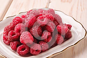 Raspberry fruits in white plate, healthy pile of summer berries on wooden background