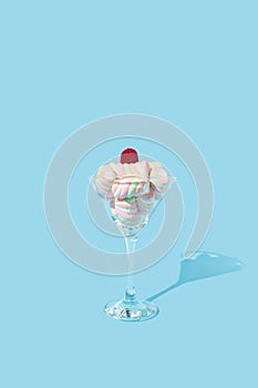 Raspberry gummy candy on the top of pile of marshmellows in cocktail glass on pastel blue background. Sweet food and drink concept