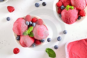 Raspberry ice cream scoop with fresh raspberries and blueberries in bowl