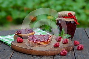 Raspberry jam with fresh raspberries and bread slices on a wooden table