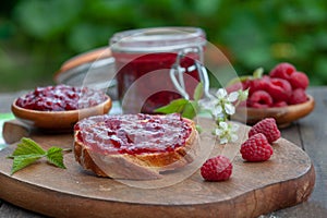 Raspberry jam with fresh raspberries and bread slices on a wooden table