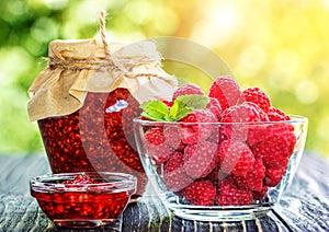 Raspberry jam and fresh raspberry on a wooden table outd