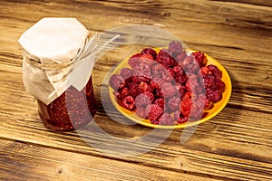 Raspberry jam in glass jar and fresh raspberries on wooden table