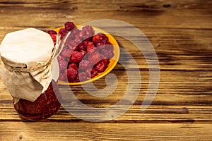 Raspberry jam in glass jar and fresh raspberries on wooden table