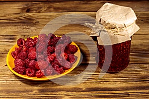 Raspberry jam in glass jar and fresh raspberries on wooden table