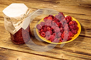 Raspberry jam in glass jar and fresh raspberries on wooden table