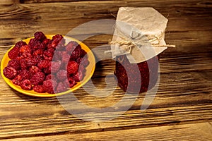 Raspberry jam in glass jar and fresh raspberries on wooden table