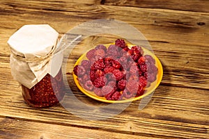 Raspberry jam in glass jar and fresh raspberries on wooden table