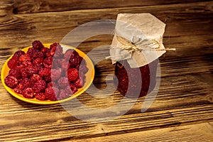 Raspberry jam in glass jar and fresh raspberries on wooden table