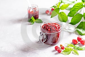 Raspberry jam in a glass jar with fresh raspberry berries on a light concrete background. Copy space