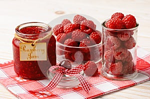 Raspberry jam in glass jar and raspberries.