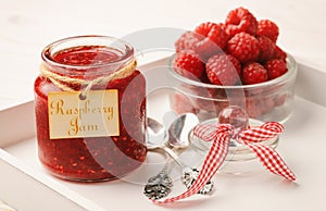 Raspberry jam in glass jar and raspberries.