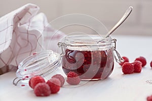 Raspberry jam in a glass jar on white table