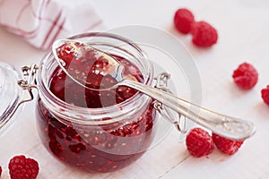 Raspberry jam in a glass jar on white table