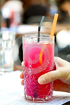 Raspberry lemonade. Hand holding a glass of raspberry ice tea with lemon and ice cubes. Cold refreshing pink cocktail in a high