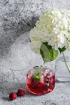 Raspberry, peach, mint cocktail lemonade refreshing drink and flowers on a gray background