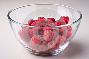 Raspberry red berries in transparent glass bowl plate tasty sweet bright on white background copy space macro