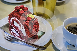 Raspberry roll cake and a cup of black coffee on a table in a cafe