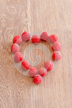 Raspberry in a shape og heart on wooden background