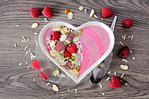 Raspberry smoothie in a heart bowl with superfoods, above on wood