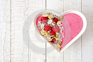 Raspberry smoothie in a heart bowl with superfoods over white wood.