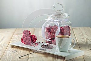 Raspberry truffle balls on a saucer next to a jar of candy and a Cup of coffee
