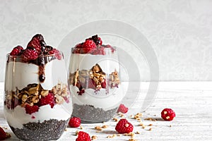 Raspberry yogurt parfait in glasses with chocolate, granola and chia seeds