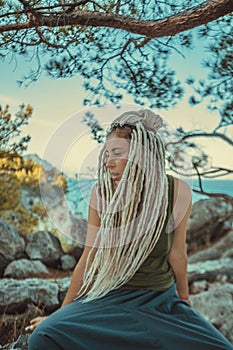 a Rastafarian girl with dreadlocks sits and smokes on a stone