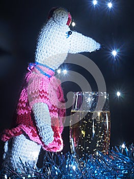 Rat doll with a glass of sparkling wine on the background of Christmas lights garland. The symbol of the new year according to the