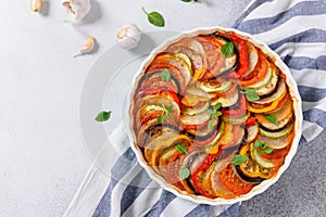 Ratatouille casserole on white background. Colorful layers of fresh summer vegetables: zucchini, eggplant, tomatoes and potatoes.