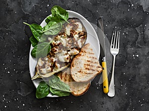 Ratatouille stuffed baked eggplant with mozzarella cheese, spinach and grilled bread on a dark background, top view