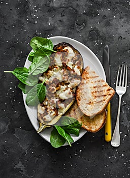 Ratatouille stuffed baked eggplant with mozzarella cheese, spinach and grilled bread on a dark background, top view
