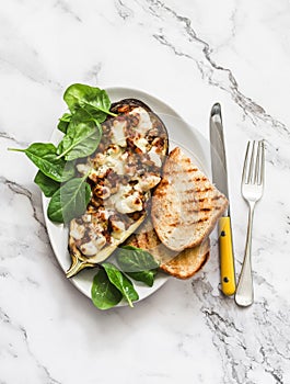 Ratatouille stuffed baked eggplant with mozzarella cheese, spinach and grilled bread on a light background, top view. Delicious